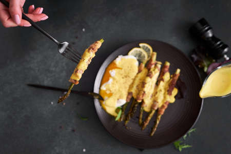 baked aspargus covered with bacon and poached eggs on a black ceramic plateの写真素材