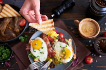 Tasty breakfast - fried egg toasts, bacon, tomatoes on wooden kitchen tableの写真素材