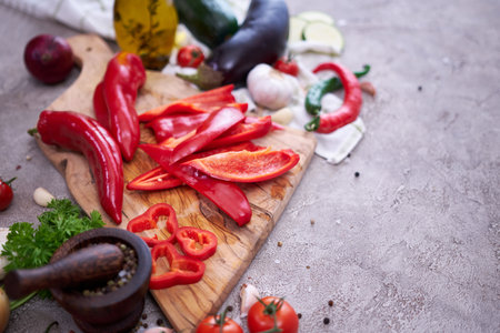 red pepper on wooden cutting board and vegetables at domestic kitchenの写真素材
