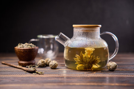 Teapot and glass cup with blooming tea flower inside on a wooden tableの写真素材