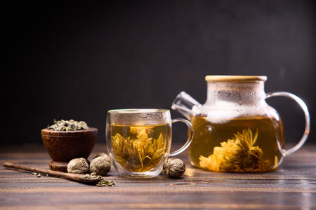 Teapot and glass cup with blooming tea flower inside on a wooden tableの写真素材