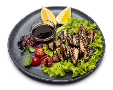 sliced pieces of Organic grilled Tuna Steak on black ceramic serving dish with salad on a tableの写真素材