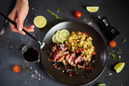 Sliced Organic grilled Tuna fillet covered with sesame seeds and salsa on black ceramic plate