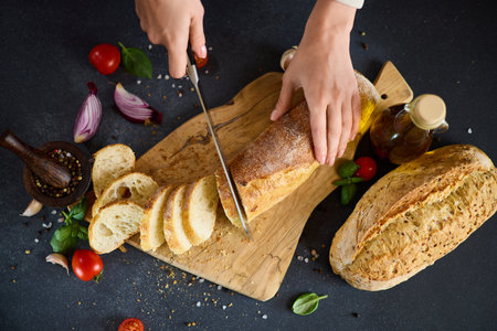 chef cutting Fresh bread on wooden cutting board on kitchen tableの写真素材