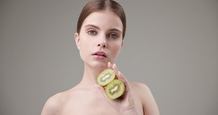 Beauty, health, cosmetics, anti-aging therapy and skin care concept - young beautiful brunette Caucasian woman holding half a kiwi in her hands, concept of vitamins, freshness, fruit powerの写真素材
