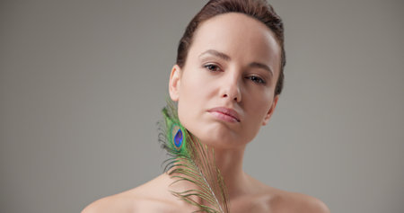 Beauty, health, cosmetics, anti-aging therapy and skin care concept - young beautiful brunette Caucasian woman holding a colorful peacock feather, concept of tenderness, softness and lightnessの写真素材