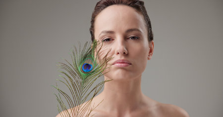 Beauty, health, cosmetics, anti-aging therapy and skin care concept - young beautiful brunette Caucasian woman holding a colorful peacock feather, concept of tenderness, softness and lightnessの写真素材