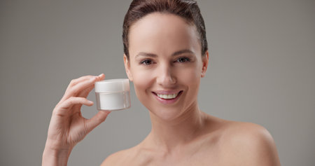 Beauty, health, cosmetics, anti-aging therapy and skin care concept - young beautiful brunette Caucasian woman holding a jar of moisturizer in her hands and looking at the cameraの写真素材