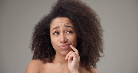 Beauty and healthcare - beautiful African American woman with curly afro hairstyle and clear, healthy skin looking around with doubt and distrust, thinking through choices or optionsの写真素材