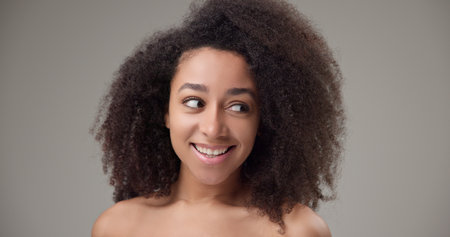 Beauty and Healthcare - Beautiful African American woman with curly afro hairstyle and clear, healthy skin looks playfully to the side with a bright toothy smileの写真素材