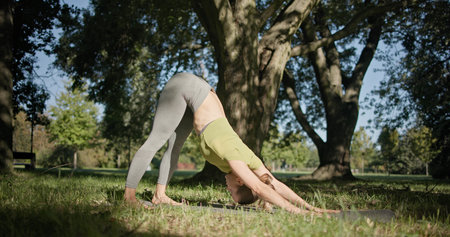 young beautiful girl doing yoga in park among trees in clearing on summer day