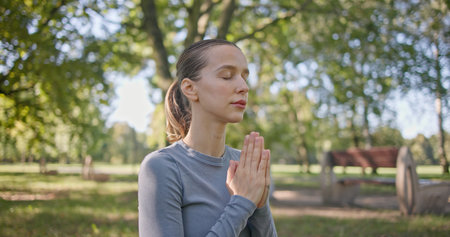 A young girl practices yoga in the park and meditates in the lotus position among the trees in a...