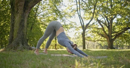 young beautiful white girl doing yoga in park among trees in clearing on summer day