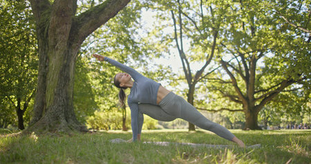 young beautiful girl doing yoga in park among trees in clearing on summer dayの写真素材