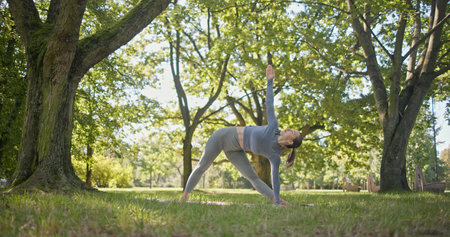 young beautiful white girl doing yoga in park among trees in clearing on summer dayの写真素材