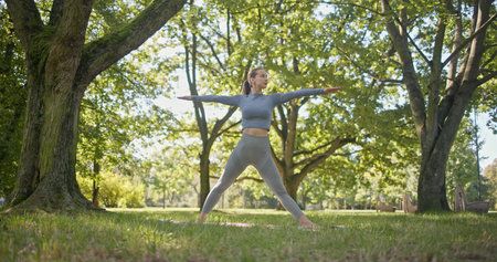 young beautiful girl doing yoga in park among trees in clearing on summer dayの写真素材