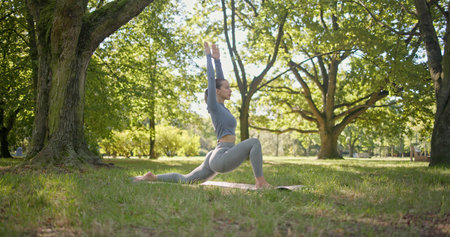 young beautiful girl doing yoga in park among trees in clearing on summer dayの写真素材