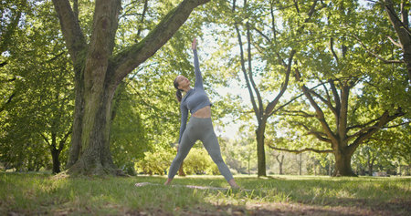 young beautiful girl doing yoga in park among trees in clearing on summer dayの写真素材