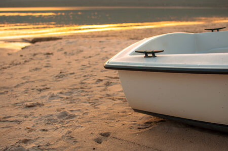 the stern of a small boat on the beach in a spring sunsetの写真素材