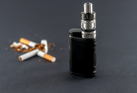 Closeup of e-cigarette and broken cigaretteson dark background