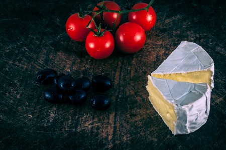 Closeup of brie cheese, black olives and cherry tomatoes on wooden chopping boardの写真素材