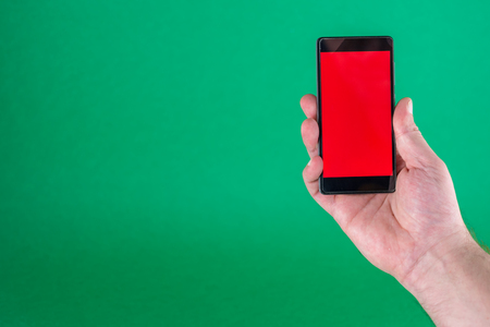 Closeup of male hand with a red screen smartphone on green backgroundの写真素材
