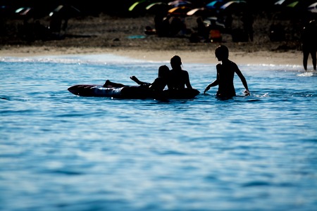 Silhouette of children play on the inflatable beach mattress in the sea in summer morning on the...