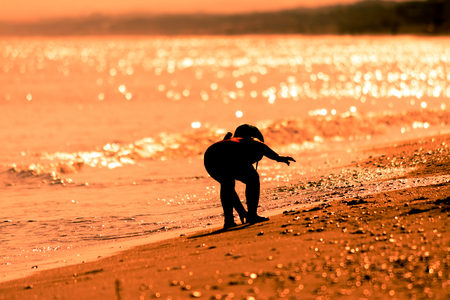 silhouette of little girl playing on the beach at sunsetの写真素材