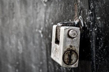 Detail of old padlock on a dirty, metallic and black doorの写真素材