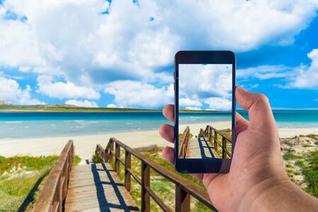 Hand taking picture with smartphone on the sardinian beach of La Pelosa, in Stintino