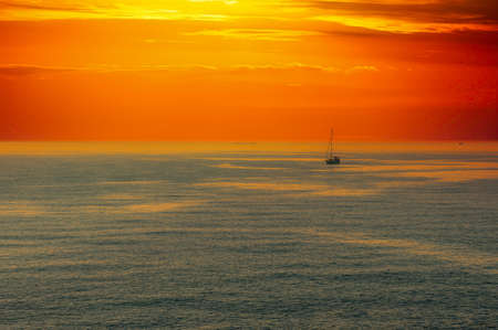 seascape at sunset with dramatic red sky and sail boatの写真素材