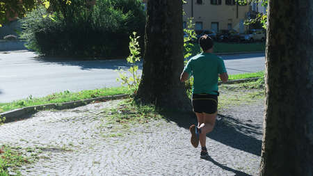 Young sport man in motion between trees outdoors in the city.