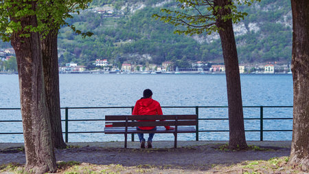Man sitting on a bench while looking away to horizon over Como lake.