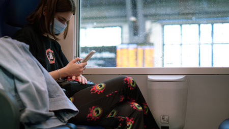 MILANO - ITALY - 19 JUNE 2021: Woman passenger using mobile phone with face covering on italian train.のeditorial素材