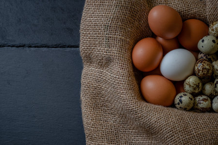 Fresh chicken and quail eggs in a basket on a sack, wooden table.Selective focus