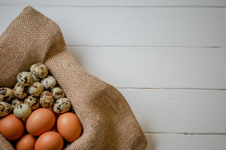 Fresh chicken and quail eggs in a basket on a sack, wooden table.Selective focusの写真素材