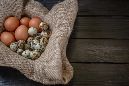 Fresh chicken and quail eggs in a basket on a sack, wooden table.Selective focusの写真素材