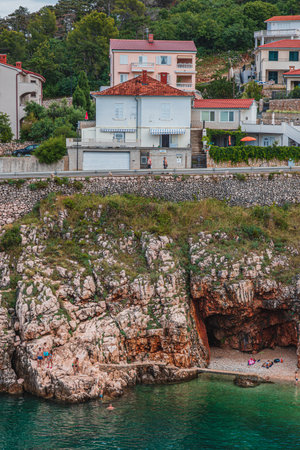 Huge rocks with greenery hang over a small beach Vrbnik Croatia 27.06.2024の写真素材
