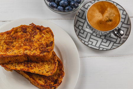 French toast on a white plate with blueberries and coffee for breakfast