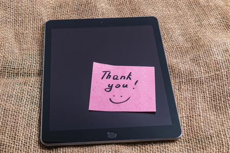 Pink thank you note on tablet screen on knitted background close up