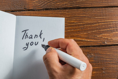 A person is writing a thank you note on a piece of paper on a wooden tableの写真素材