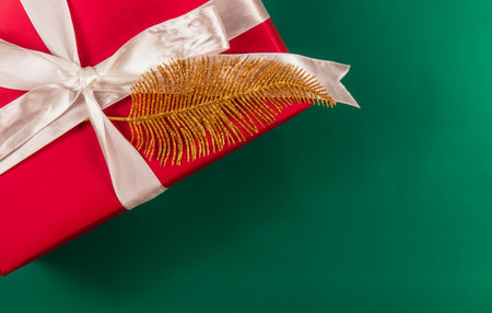 A red gift box with a white bow and gold leaf on a green background.