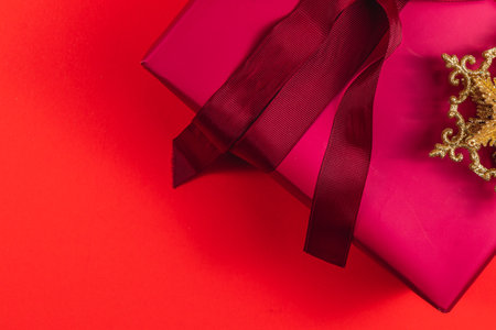 Festive gift box with bow and golden decorative star on red backgroundの写真素材