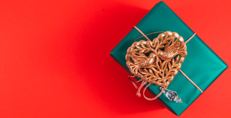Banner green Christmas gift box with gold heart decoration on red background
