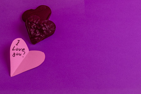 Dark chocolate heart with paper and the phrase I love you on a purple background