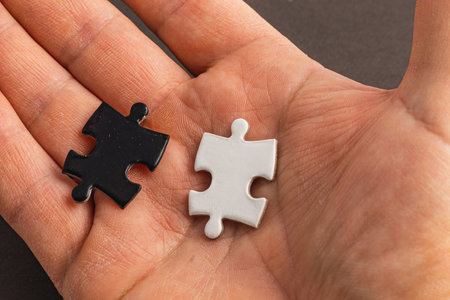 A hand holding two puzzle pieces one white and one black, difficult choice