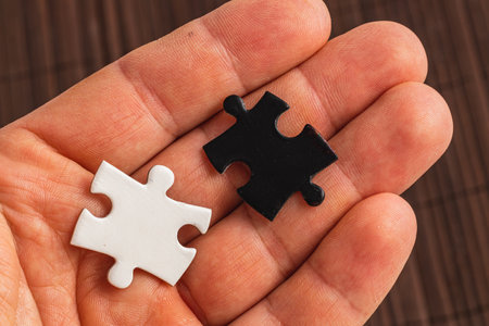 A hand holding two puzzle pieces one white and one black, difficult choice
