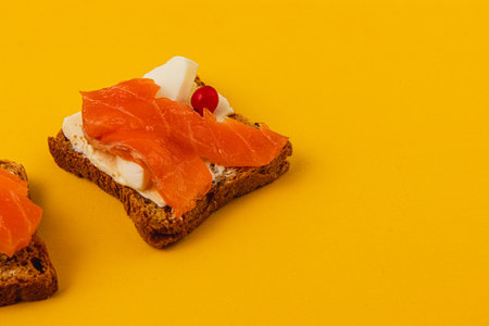Toasts with butter, salmon and cranberries on a yellow background close upの写真素材
