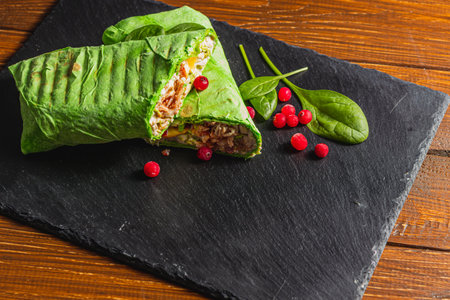 Homemade shawarma with spinach filled with chicken, vegetables on a stone boardの写真素材