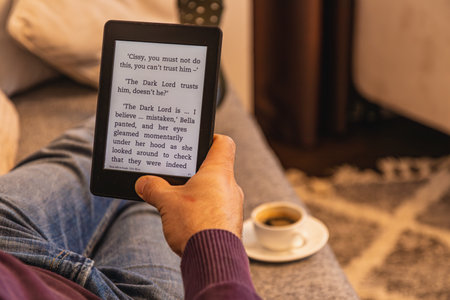 Relaxing at home, a person is engrossed in an e book, experiencing an enchanting narrative while enjoying a warm beverage beside them. The cozy atmosphere enhances the reading experience.の写真素材